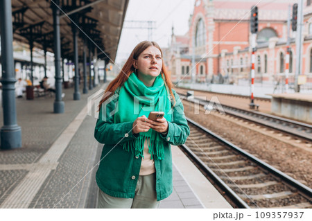 Young worried woman traveler with small backpack on the railway station, 30s redhead women waiting for train. Tourism, solo vacation 109357937