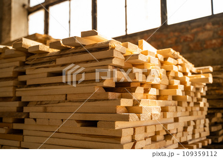 Stacked raw wooden planks at a indoor lumber warehouse. Background of boards. Raw wood drying in the lumber warehouse. Wood industry. Stacked raw wooden planks at a indoor lumber warehouse. Background of boards. Raw wood drying in the lumber warehouse. Wood industry. 109359112