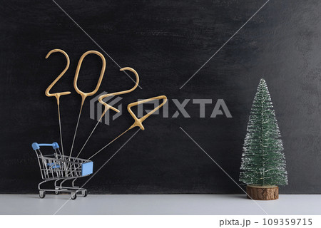 Shopping cart with golden number 2024 and miniature Christmas tree on black background. New year shopping. Shopping cart with golden number 2024 and miniature Christmas tree on black background. New year shopping. 109359715