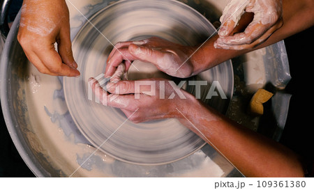 Close-up of a female potter's hands moulding and shaping a stunning piece of white clay pottery. The hands of a mentor helping a student. Open lesson. The concept of manual labour, art and craft. Close-up of a female potter's hands moulding and shaping a stunning piece of white clay pottery. The hands of a mentor helping a student. Open lesson. The concept of manual labour, art and craft. 109361380