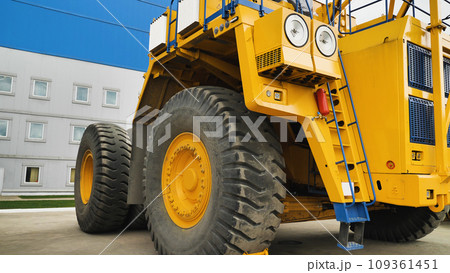 A large dump truck without a body. A huge dump truck standing near the factory walls. A yellow dump truck. Close-up. A large dump truck without a body. A huge dump truck standing near the factory walls. A yellow dump truck. Close-up. 109361451