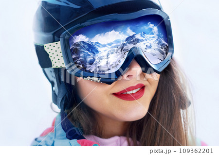 Portrait of young woman at the ski resort on the background of mountains and blue sky.A mountain range reflected in the ski mask Portrait of young woman at the ski resort on the background of mountains and blue sky.A mountain range reflected in the ski mask 109362201