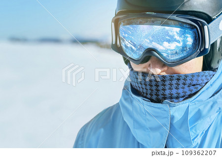 Close up of the ski goggles of a man with the reflection of snowed mountains. A mountain range reflected in the ski mask. Man on the background blue sky. Wearing ski glasses. Winter Sports. Close up of the ski goggles of a man with the reflection of snowed mountains. A mountain range reflected in the ski mask. Man on the background blue sky. Wearing ski glasses. Winter Sports. 109362207
