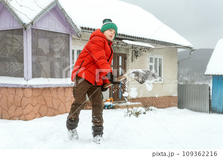 Little boy in warm puffy jacket and knitted hat with shovel cleans the snow in the yard of house. Snowy winter, cold weather Little boy in warm puffy jacket and knitted hat with shovel cleans the snow in the yard of house. Snowy winter, cold weather 109362216
