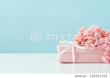 Pink gift box with tender pink carnation flowers. Blue background. Gift or holiday concept. Mothers Day, birthday wedding or St Valentines day with copy space. Minimal 109362308