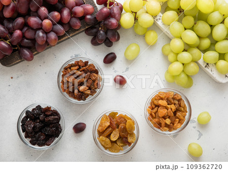 Dried green and red dark raisins with ripe raw grapes on light background. Dried green and red dark raisins with ripe raw grapes on light background. 109362720