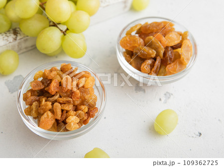 Sweet dried green raisins in glass bowl with ripe grapes in wooden box 109362725