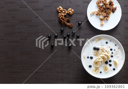 Healthy breakfast concept with oatmeal porridge with bananas, milk, blueberries,  nuts, raisins, chia seeds and currants. Top view. Super food 109362801