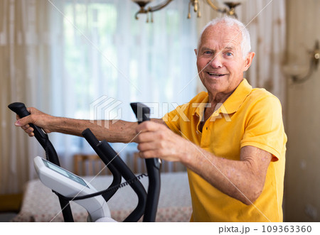 Senior man with elliptical trainer at home 109363360