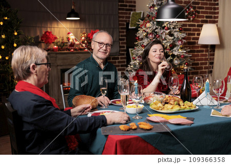 Old person at table on xmas with family eating traditional meal and celebrating christmas holiday at home. Senior people hosting festive xmas dinner event during winter season. 109366358