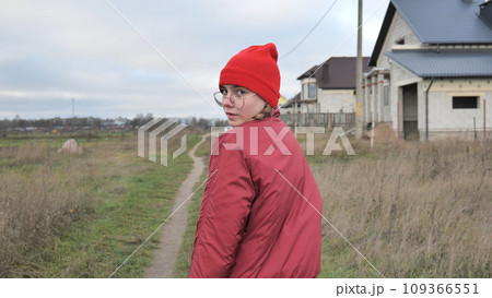 A sad teenage girl in red clothes is walking down the street. View from the back. 109366551