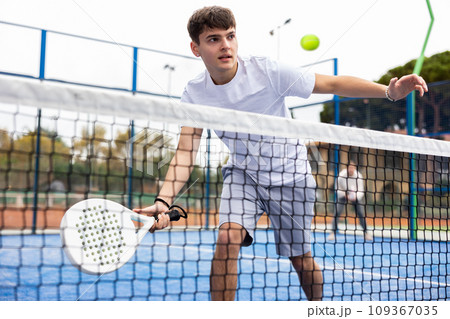 Young focused guy playing paddle tennis outdoors 109367035