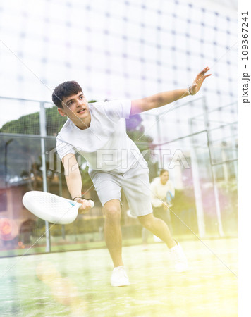 Sportive young man playing padel with partner outdoors. View through tennis net 109367241