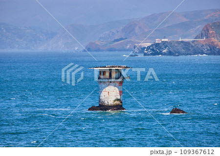 Abandoned lighthouse structure in middle of bay with distant mountainous coastline 109367612