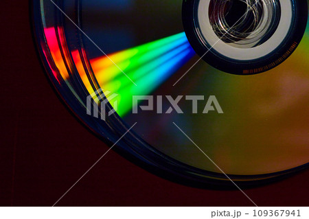 Stacked CDs in dark setting with cone of rainbow colored light shaft across silvery surface Stacked CDs in dark setting with cone of rainbow colored light shaft across silvery surface 109367941