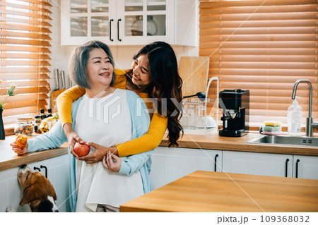 In the kitchen, an old mother receives a loving embrace from her cute young daughter. This heartwarming portrait captures the essence of family togetherness and care. In the kitchen, an old mother receives a loving embrace from her cute young daughter. This heartwarming portrait captures the essence of family togetherness and care. 109368032