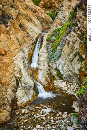 Small creek between cliff walls flowing into shallow pool of water with large stones Small creek between cliff walls flowing into shallow pool of water with large stones 109368343