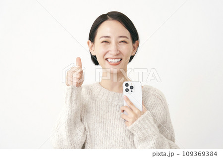 スマホを持ってグッドサインをするミドルエイジの女性 白背景 スマホを持ってグッドサインをするミドルエイジの女性 白背景 109369384
