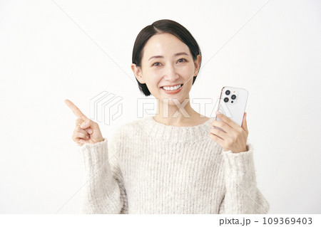 スマホを持って左側を指差すミドルエイジの女性 白背景 スマホを持って左側を指差すミドルエイジの女性 白背景 109369403