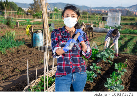 Woman gardener wearing face mask for prevention corona virus and holding shovel in garden Woman gardener wearing face mask for prevention corona virus and holding shovel in garden 109371573