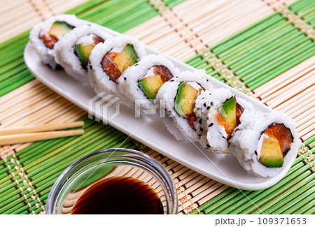On table there is plate with set of sushi - uramaki rolls california roll with chees On table there is plate with set of sushi - uramaki rolls california roll with chees 109371653