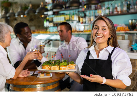 Cheerful smiling female waiter holding served tray meeting visitors at bar 109371763