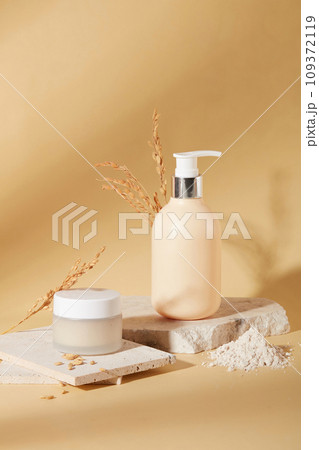 Front view of a jar of lotion and a bottle of shower gel are placed on a podium with rice bran powder on a beige background. Skin care with natural ingredients. Front view of a jar of lotion and a bottle of shower gel are placed on a podium with rice bran powder on a beige background. Skin care with natural ingredients. 109372119
