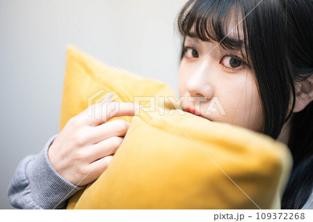 部屋着でクッションを持ちながらベットに座っている若い女性 109372268