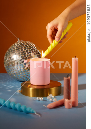 Close up of woman hand lighting candles on colorful background. Candles, pearls and a disco ball decorated on the table. Party atmosphere. Creative space for ads. 109373688