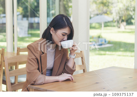 Beauty woman drinking black coffee in coffee shop holding freshness cup. Coffee lover. Asian Woman drink black coffee hand holding cup at green garden cafe. Young woman smile face love drink coffee 109375137