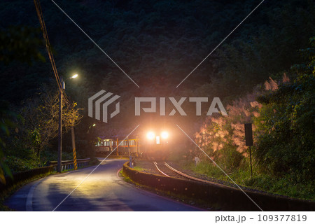 A yellow diesel train passes through the village at night with its lights on. A yellow diesel train passes through the village at night with its lights on. 109377819