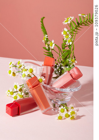 Four unbranded lipsticks are displayed alongside daisies and fern leaves on a pink background. Concept of homemade cosmetics with natural ingredients. Four unbranded lipsticks are displayed alongside daisies and fern leaves on a pink background. Concept of homemade cosmetics with natural ingredients. 109379026