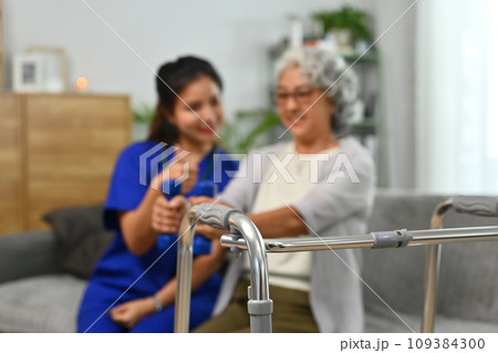 A metal walker on background of caregiver helping senior female patient in at retirement home 109384300