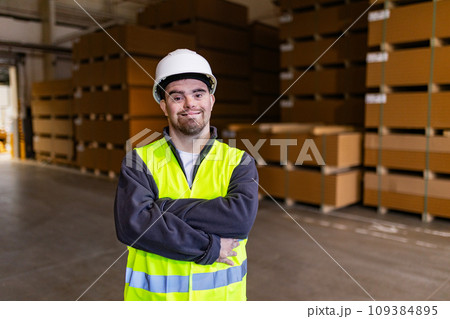 Portrait of young man with Down syndrome working in factory, warehouse. Concept of workers with disabilities, support in workplace. Portrait of young man with Down syndrome working in factory, warehouse. Concept of workers with disabilities, support in workplace. 109384895