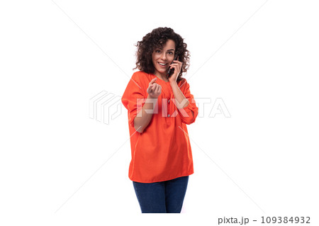 young caucasian business woman with a curly hairstyle dressed in an orange shirt speaks on the phone young caucasian business woman with a curly hairstyle dressed in an orange shirt speaks on the phone 109384932