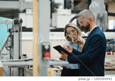 Female engineer and male production manager standing in modern industrial factory, talking about production. Manufacturing facility with robotics and automation. 109384942