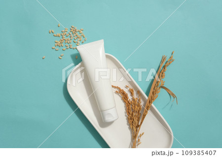 Cosmetic tube without label decorated with wheat ears on a dish. A handful of wheat seeds featured. Empty label tube for natural beauty product advertising 109385407