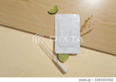 Unbranded mask package placed on wooden surface, displayed with slices of lime. Rice bran powder contained inside a test tube. Skin care product concept Unbranded mask package placed on wooden surface, displayed with slices of lime. Rice bran powder contained inside a test tube. Skin care product concept 109385408