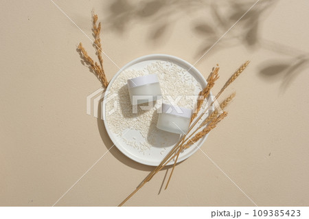 Two empty label jars are arranged on a round dish with a lot of rice and wheat ears. Natural soft shadow. Rice water helps to lighten skin or reduce dark patches Two empty label jars are arranged on a round dish with a lot of rice and wheat ears. Natural soft shadow. Rice water helps to lighten skin or reduce dark patches 109385423