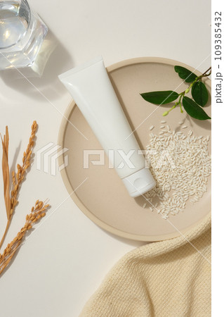 Round dish featured a beauty tube with rice and green leaves. Arranged with a towel, wheat ears and a glass of water. Mockup tubes for skin care cosmetic Round dish featured a beauty tube with rice and green leaves. Arranged with a towel, wheat ears and a glass of water. Mockup tubes for skin care cosmetic 109385432
