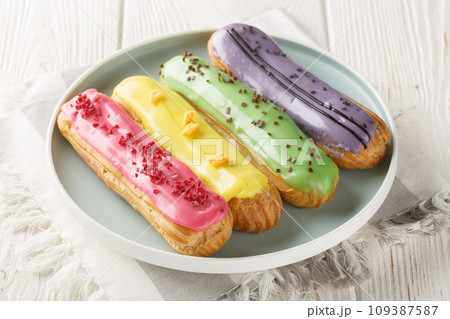 Various glazed sweet eclairs with with berry tastes closeup on plate. Horizontal 109387587