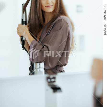 Woman straightening hair with straightener Woman straightening hair with straightener 109387950