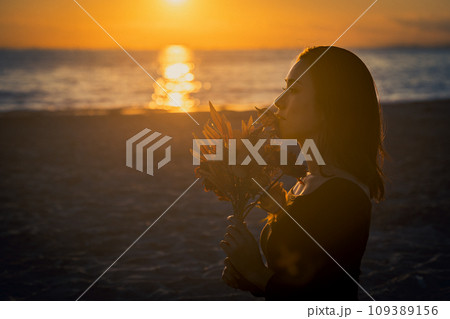 海辺の夕景をバックに花を持つ女性 海辺の夕景をバックに花を持つ女性 109389156