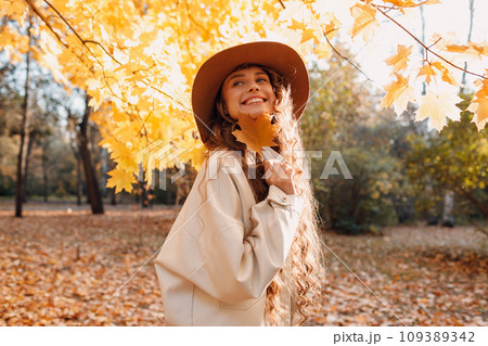 Smiling young woman portrait in the autumn forest with the yellow leaves at sunset time Smiling young woman portrait in the autumn forest with the yellow leaves at sunset time 109389342