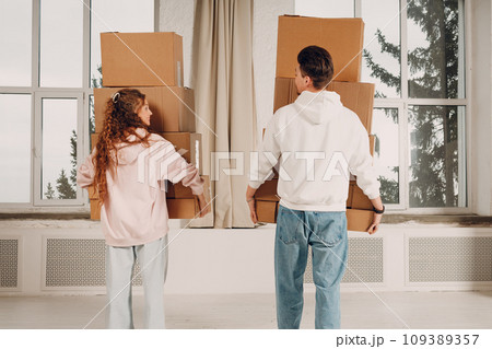 Happy young family couple man and woman moving with cardboard boxes to new estate home apartment. Rear back view. 109389357