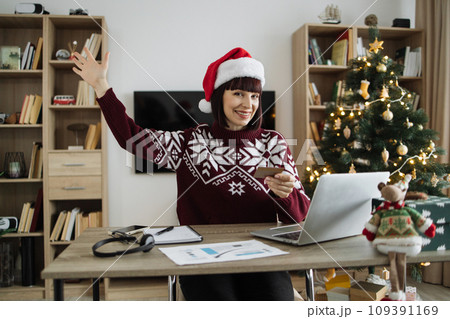 Woman in Santa hat raising palm hand while looking at laptop with credit card. 109391169