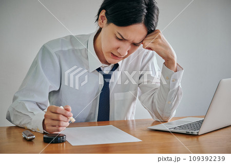 しかめっ面の表情で書類に印鑑を押す若い男性 109392239