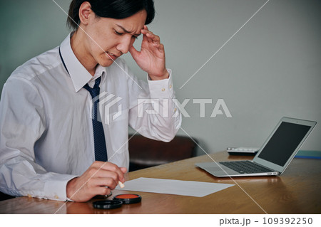 しかめっ面の表情で書類に印鑑を押す若い男性 109392250
