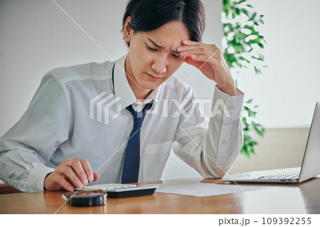 しかめっ面の表情をしながら電卓で計算をする若い男性 109392255