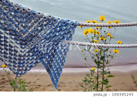 A lace wicker blanket of blue color forgotten on the ropes against the backdrop of flowers and a sandy beach A lace wicker blanket of blue color forgotten on the ropes against the backdrop of flowers and a sandy beach 109395245